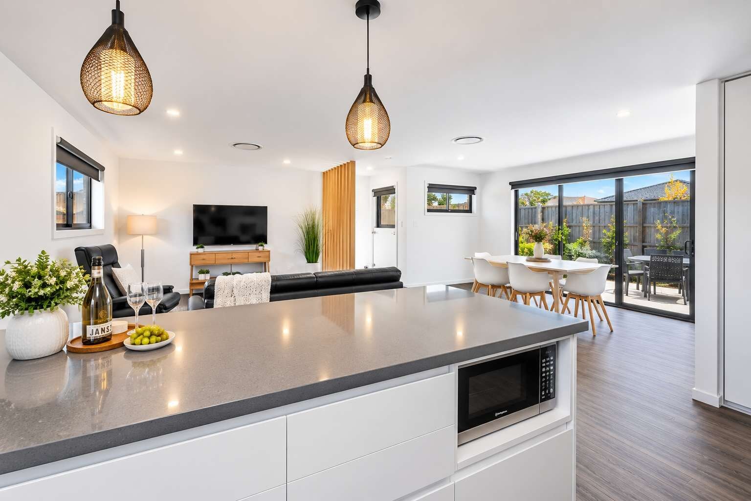 Une cuisine moderne avec un îlot central, un coin repas avec des chaises blanches et une grande fenêtre donnant sur un jardin.