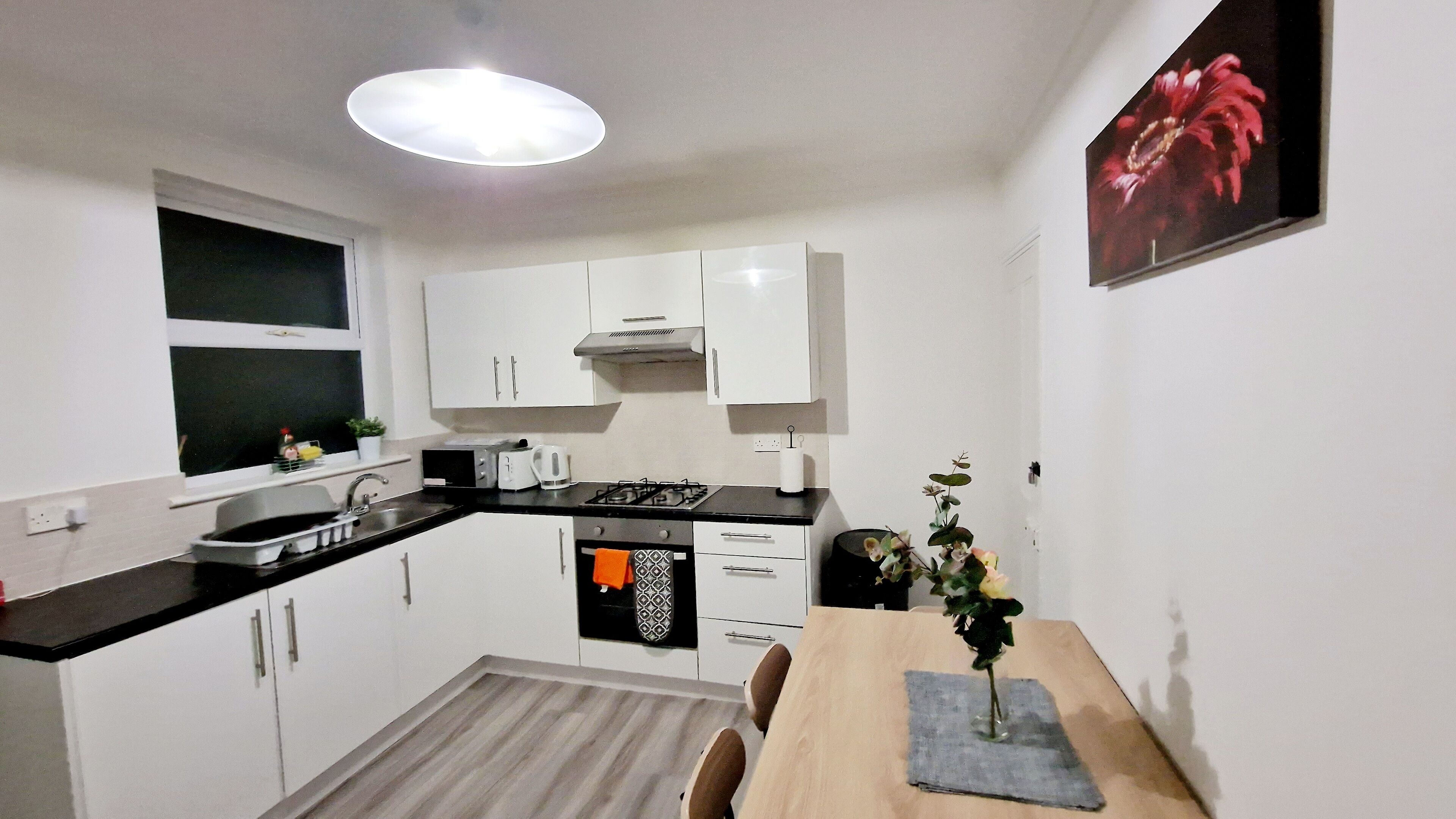 A modern kitchen with white cabinets, a black countertop, and a wooden dining table with chairs.