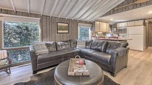 A modern living room with a sectional sofa, a coffee table, and a dining area with a kitchen in the background. - Serene and Secluded Walk Up in the Woods (Ligonier)