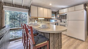 A modern kitchen with a central island, wooden cabinets, and a view of trees through the window. - Serene and Secluded Walk Up in the Woods (Ligonier)