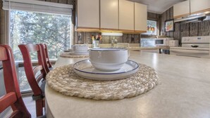 A modern kitchen with a central island, wooden chairs, and a view of the outdoors. - Serene and Secluded Walk Up in the Woods (Ligonier)