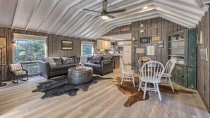 A spacious living room with a large sofa, a coffee table, and a dining area with chairs. There is a kitchen in the background with modern appliances. - Serene and Secluded Walk Up in the Woods (Ligonier)