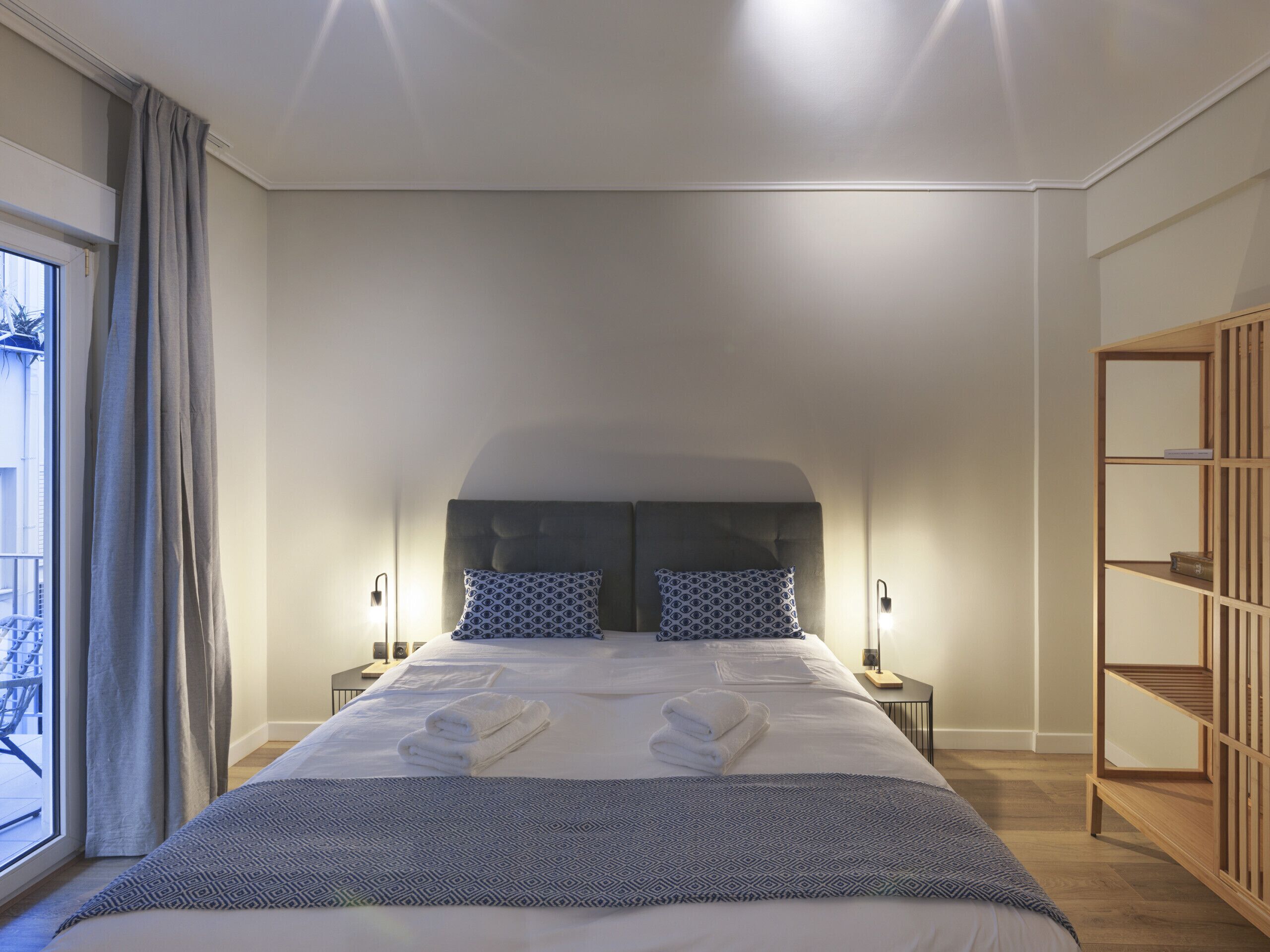 Une chambre moderne avec un grand lit, deux tables de chevet, une armoire et une vue sur l’extérieur.