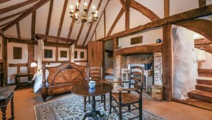A traditional room with exposed wooden beams, a large bed, a fireplace, and a chandelier. - Hell Fyre 1594 by inspirestays.com - a cottage that sleeps 2 guests in 1 bedroom (Itchingfield, nr Horsham)