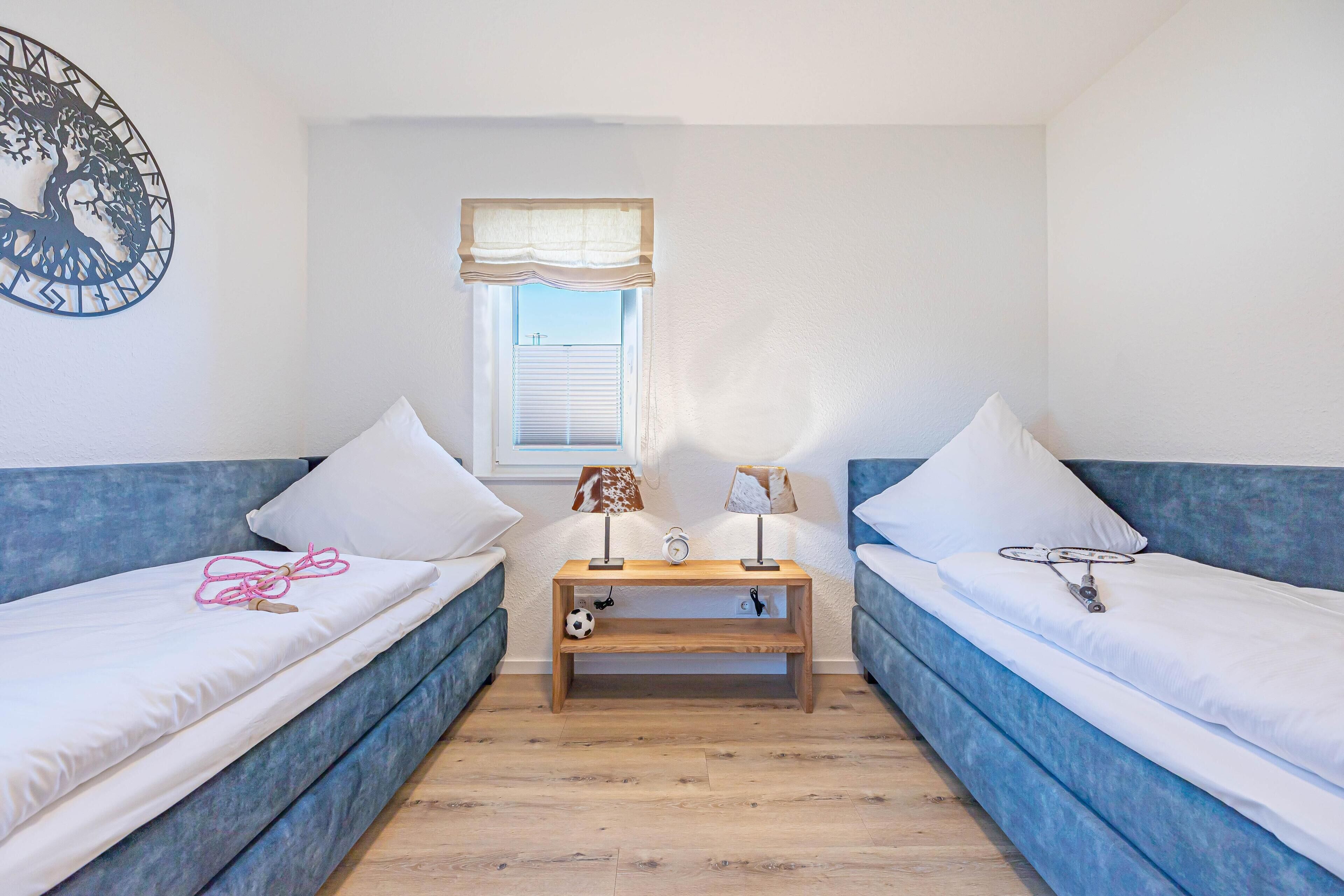 A room with two blue sofas, a wooden nightstand with a clock, and a wall decoration.