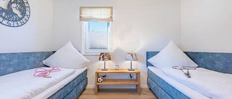 A room with two blue sofas, a wooden nightstand with a clock, and a wall decoration.