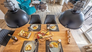 A dining area with a wooden table set for four, surrounded by black chairs. There are plates with food, a bottle of wine, and glasses. The room has a modern design with a blue sofa and a cowhide rug. - Wiking-Koje 3 - Elevator, 1st Floor, Underfloor Heating, Shower, Washing Machine (Schleswig)