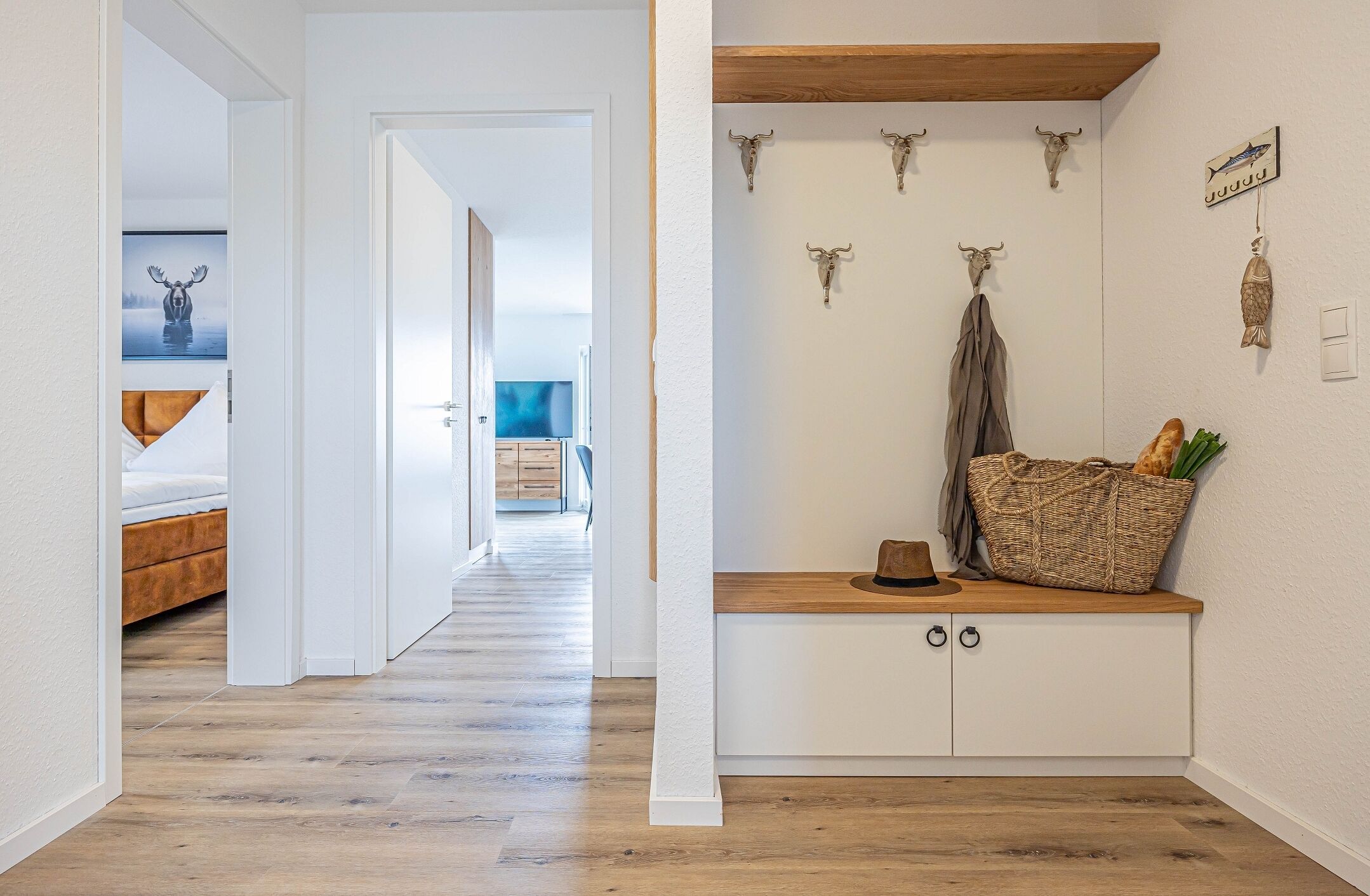 Ein Flur mit Holzboden, einem Bett, einem Fernseher im Hintergrund und einer Wand mit verzierten Schädeln und einem Korb.