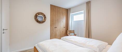 A bedroom with two beds, a wooden wardrobe, a mirror, and a window with curtains.
