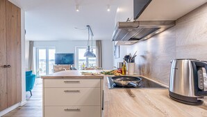 A modern kitchen with wooden cabinets, a built-in stove, and a kettle. - Wiking-Koje 8 - Accessible, Elevator, 2nd Floor, Underfloor Heating, Balcony (Schleswig)