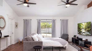 Un dormitorio con cama, sofá gris, televisión y ventilador de techo.