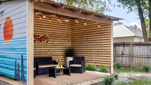 Un porche techado con listones de madera, muebles de exterior y luces colgantes.