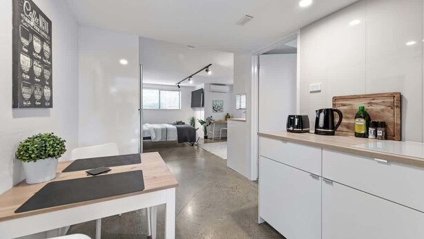 A modern kitchen with white cabinets, a wooden countertop, and a coffee station.