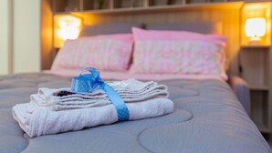 A neatly made bed with folded towels and a blue ribbon, a headboard with shelves, and two bedside lamps. - HAPPY HOUSE [7 minutes from MXP and 30 minutes from Milan] (Busto Arsizio)