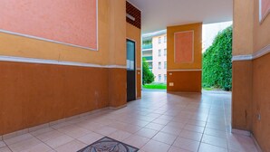 A corridor with tiled flooring and a patterned mat, leading to a door and a building with balconies. - HAPPY HOUSE [7 minutes from MXP and 30 minutes from Milan] (Busto Arsizio)