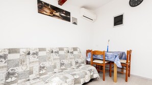 A cozy living room with a sofa, a dining table with chairs, and a clock on the wall. - Studio Nena (Rovinj)