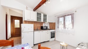 A compact kitchen with white cabinets, a coffee machine, and a small dining table with chairs. - Studio Nena (Rovinj)