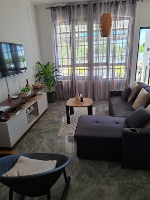 Een moderne woonkamer met een bank, een televisie, een salontafel en een potplant.