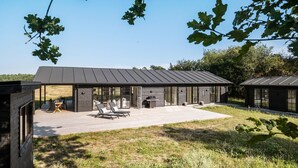 Un espace de restauration extérieur moderne, doté d’une terrasse en bois, de sièges et d’un barbecue.