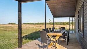 Une terrasse en bois avec une table et des chaises, donnant sur un champ verdoyant.