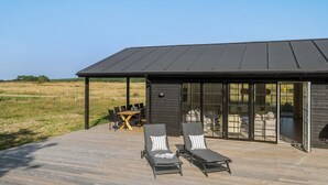 A modern outdoor lounge area with two lounge chairs, a table, and a glass-enclosed patio.