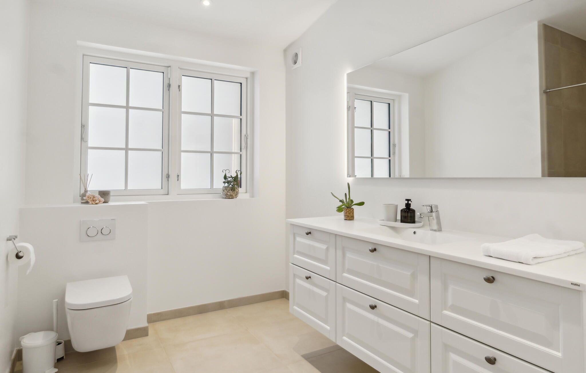 Een moderne badkamer met toilet, een wastafel met spiegel en een raam.