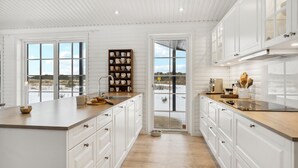 A spacious kitchen with white cabinetry, a wooden countertop, and a view of a snowy landscape through large windows.