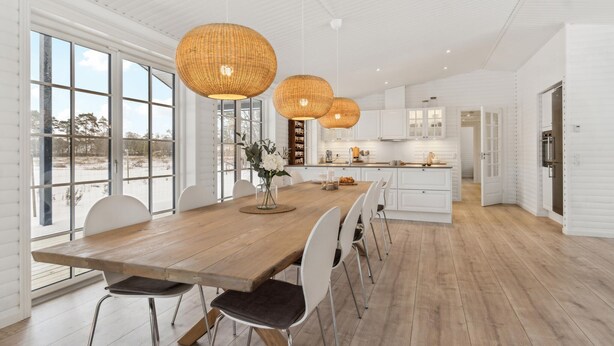 A spacious dining area with a long wooden table, white chairs, and large woven pendant lights.