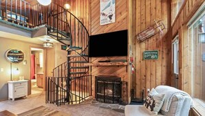 A cabin interior with a spiral staircase, a fireplace, a sofa, and a television.