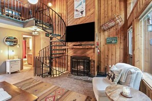L’intérieur d’une cabane comprend un escalier en colimaçon, une cheminée, un canapé et un téléviseur.