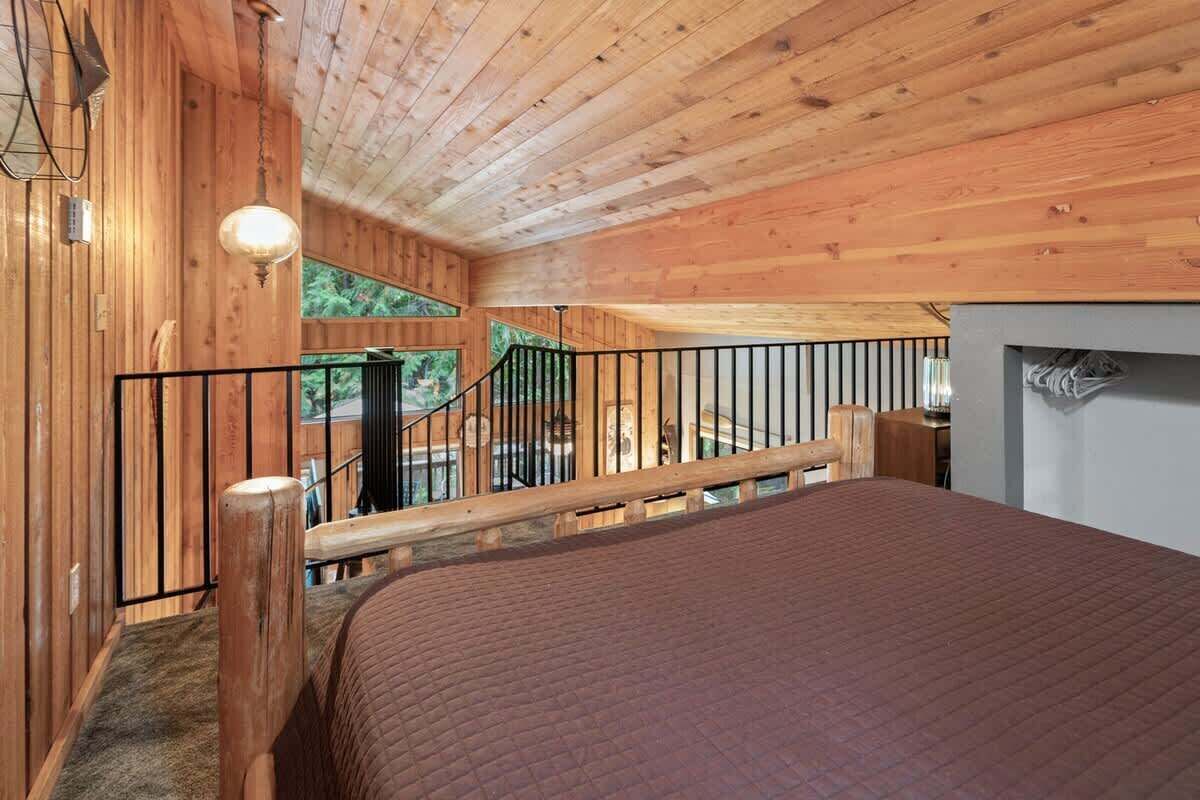 L’intérieur d’un chalet en bois, avec un lit, un escalier et une vue sur la verdure environnante.