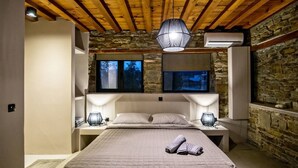 A bedroom with a large bed, two bedside tables, a stone wall, and a wooden ceiling.