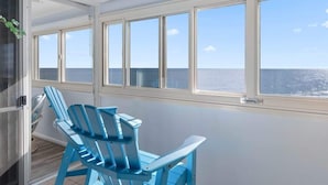 Quarto com vista para o mar, uma porta de correr e duas cadeiras azuis.