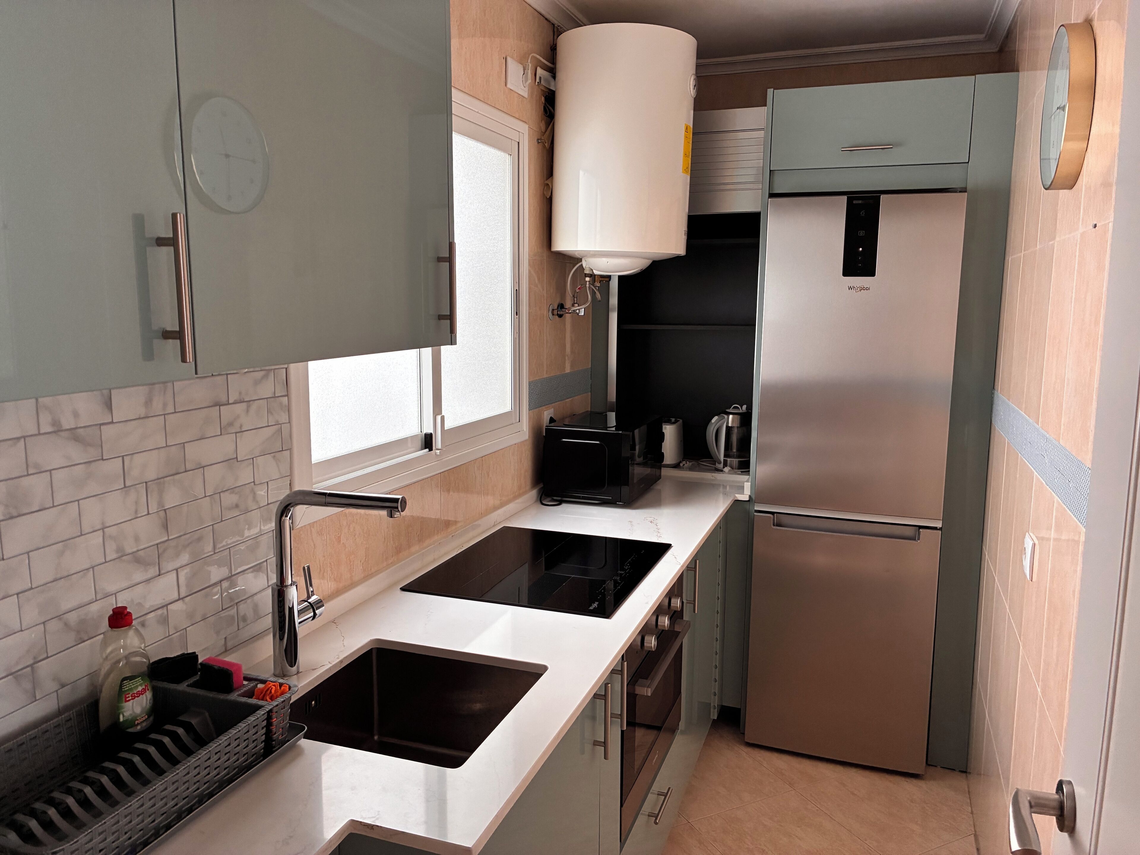 Uma cozinha compacta com geladeira de aço inoxidável, forno embutido, micro-ondas e pia com torneira moderna.