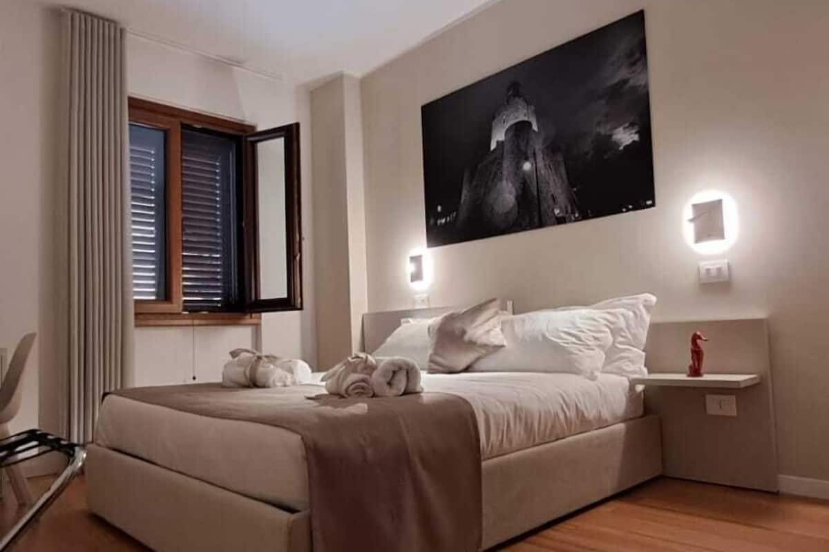 A modern bedroom with a large bed, a ceiling light, a wall-mounted TV, and a bedside table with a red object.