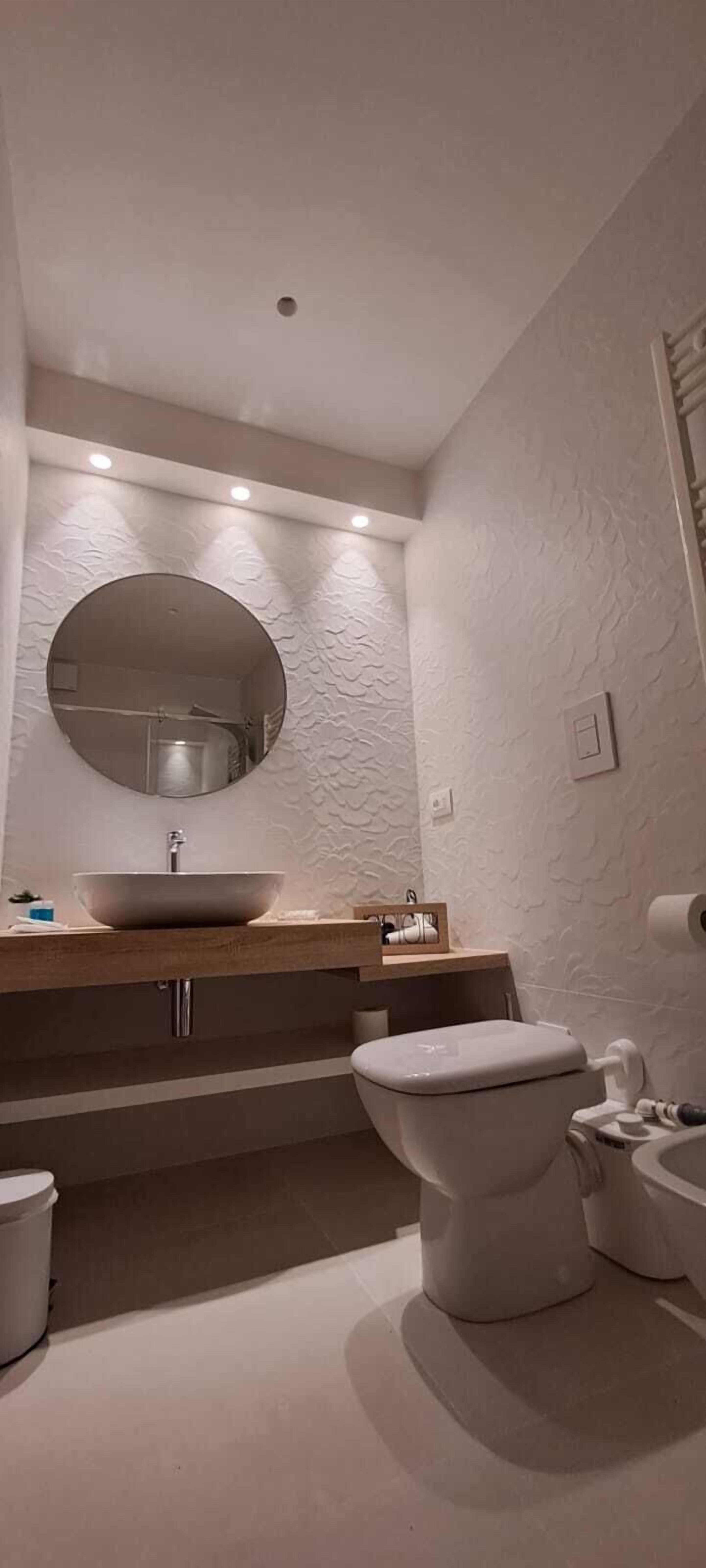 Un bagno moderno con uno specchio rotondo, un lavabo a incasso e un water.