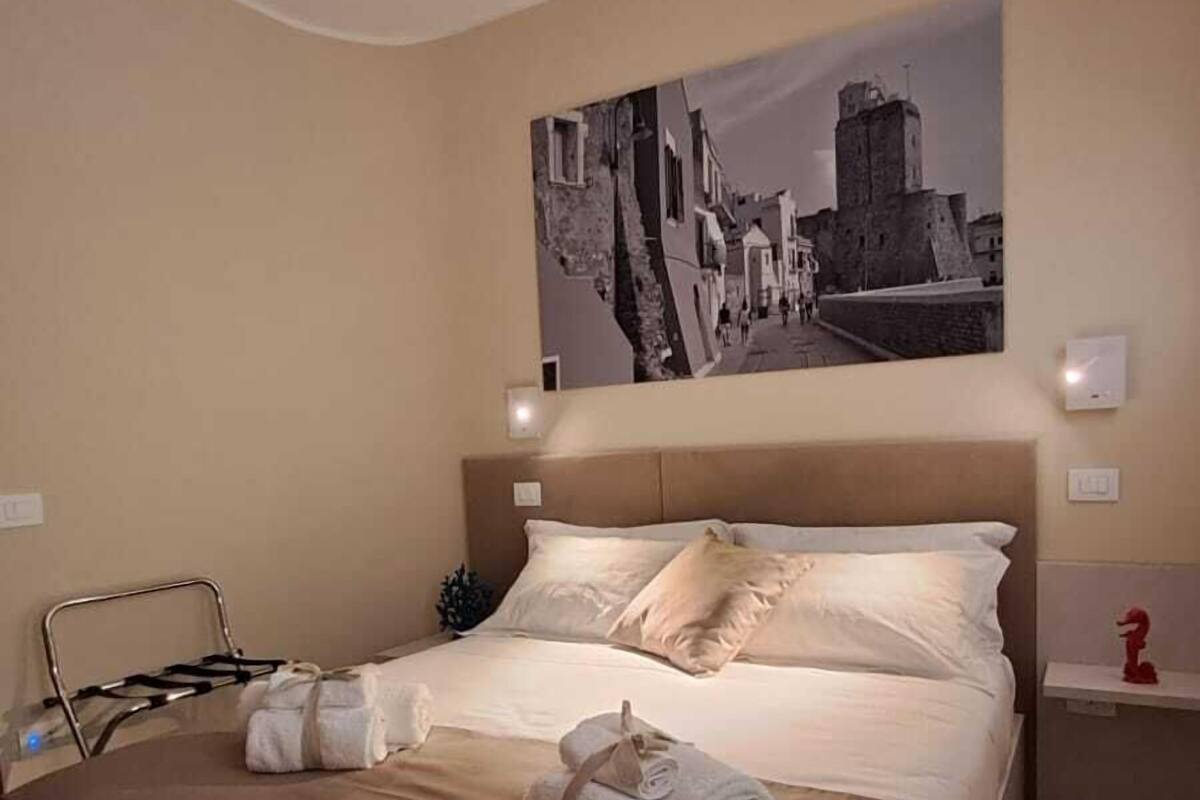 A hotel room with a bed, a headboard, a wall-mounted artwork, a bedside table, and a red decorative item.