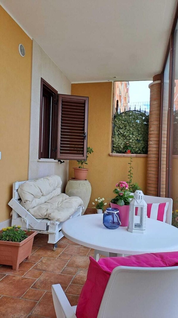 A small patio with a white table, a white chair, a sofa, and a window with a view of buildings. - B&B Tramonto Sul Mare (Termoli)