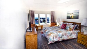 A bedroom with a large bed, a desk, a chair, a nightstand, a lamp, and a painting on the wall. - This two-bedroom, two bathroom condo has a beautiful view of the ocean, and outdoor pool. (Ocean City)
