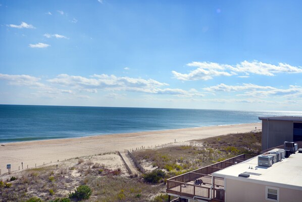 A beach view with a sandy shore, a wooden fence, and a building with air conditioning units.