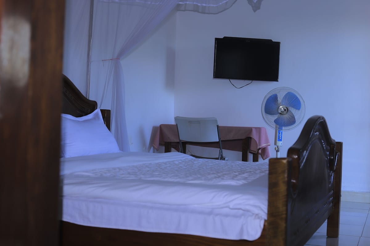Un dormitorio con cama, escritorio, silla, televisor y ventilador.