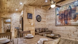 A wooden interior with a dining table set for four, a sofa, and a large abstract painting on the wall.