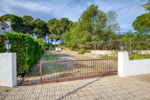 A paved pathway leading to a gated entrance with a metal fence, surrounded by lush greenery and trees. - TREBOL: Apartment in l'Escala with community pool and garden, ideal for families (L'Escala)