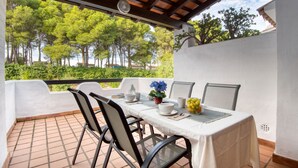 A covered outdoor dining area with a table set for two, chairs, and a view of trees. - TREBOL: Apartment in l'Escala with community pool and garden, ideal for families (L'Escala)