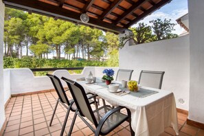 A covered outdoor dining area with a table set for two, chairs, and a view of trees.
