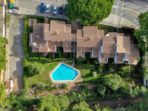 An aerial view of a residential area with multiple houses, a swimming pool, and a road with parked cars.
