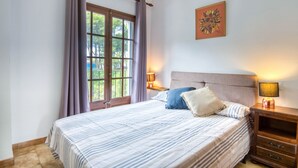 A bedroom with a bed, two bedside tables, a window with curtains, and a wall-mounted lamp. - TREBOL: Apartment in l'Escala with community pool and garden, ideal for families (L'Escala)