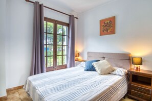A bedroom with a bed, two bedside tables, a window with curtains, and a wall-mounted lamp.