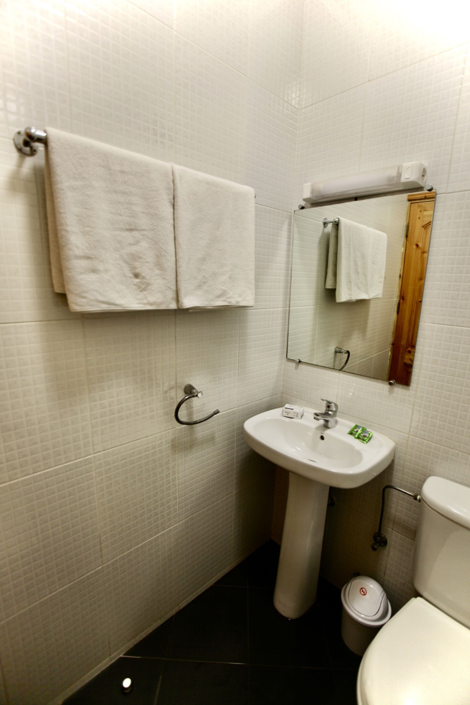 Une salle de bain avec un lavabo blanc, un miroir et des toilettes. Deux serviettes sont accrochées au mur.