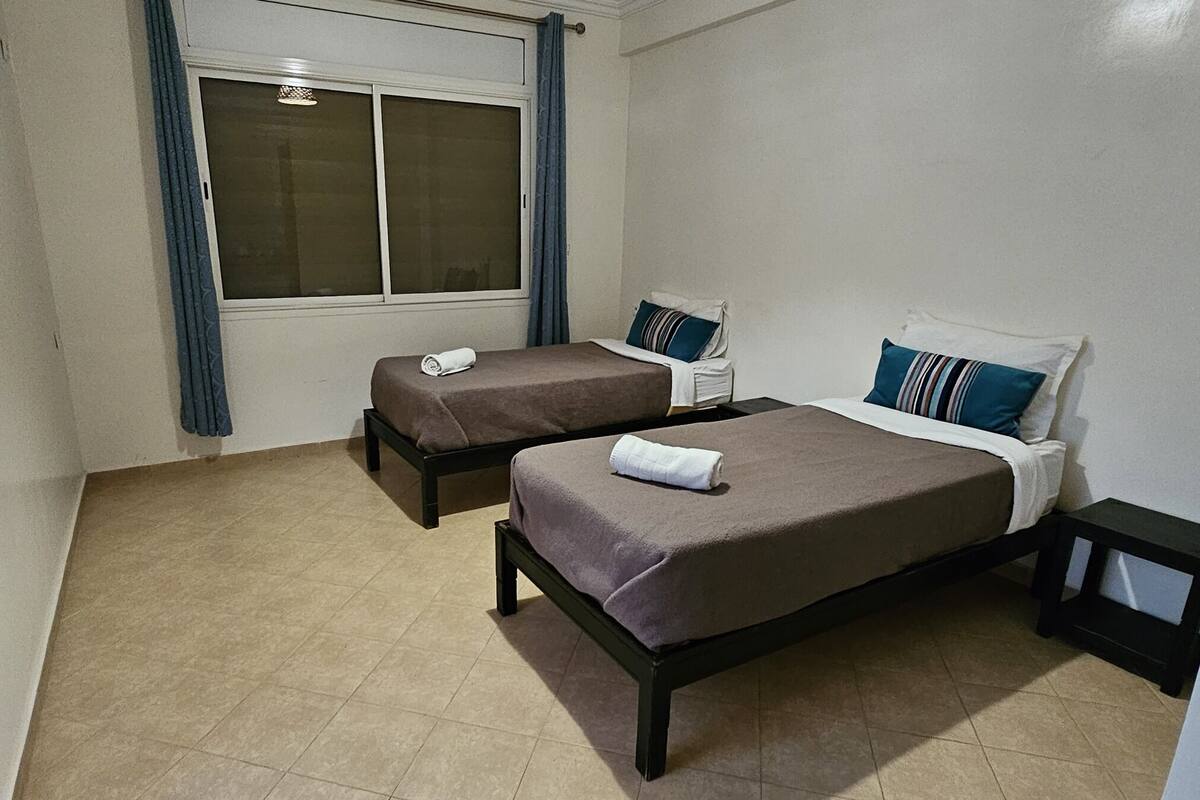 A small, clean room with two beds, a window, and a door.